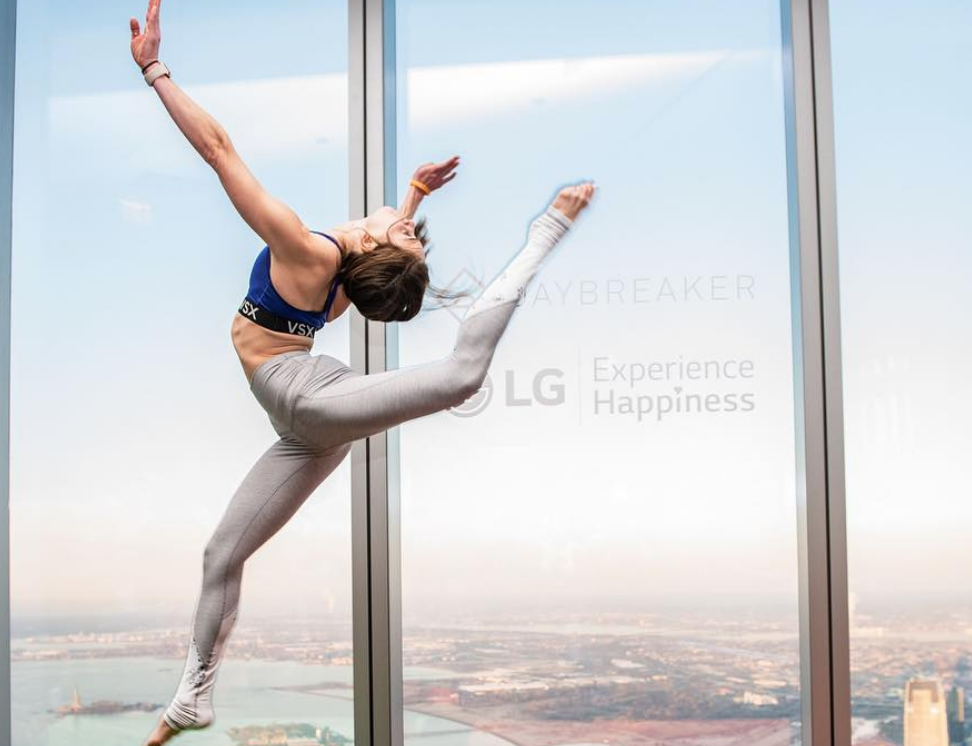 Image of a woman in workout gear doing a high kick dance move in front of a window for LG Experience Happiness