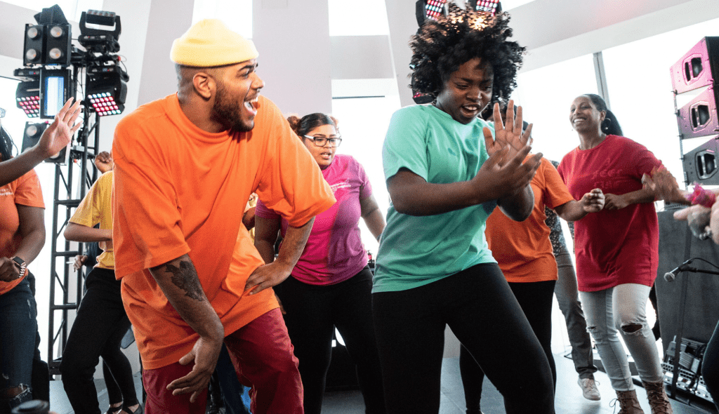 A group of young african american students in brightly colored t-shirts dancing at an LG Experience Happiness event