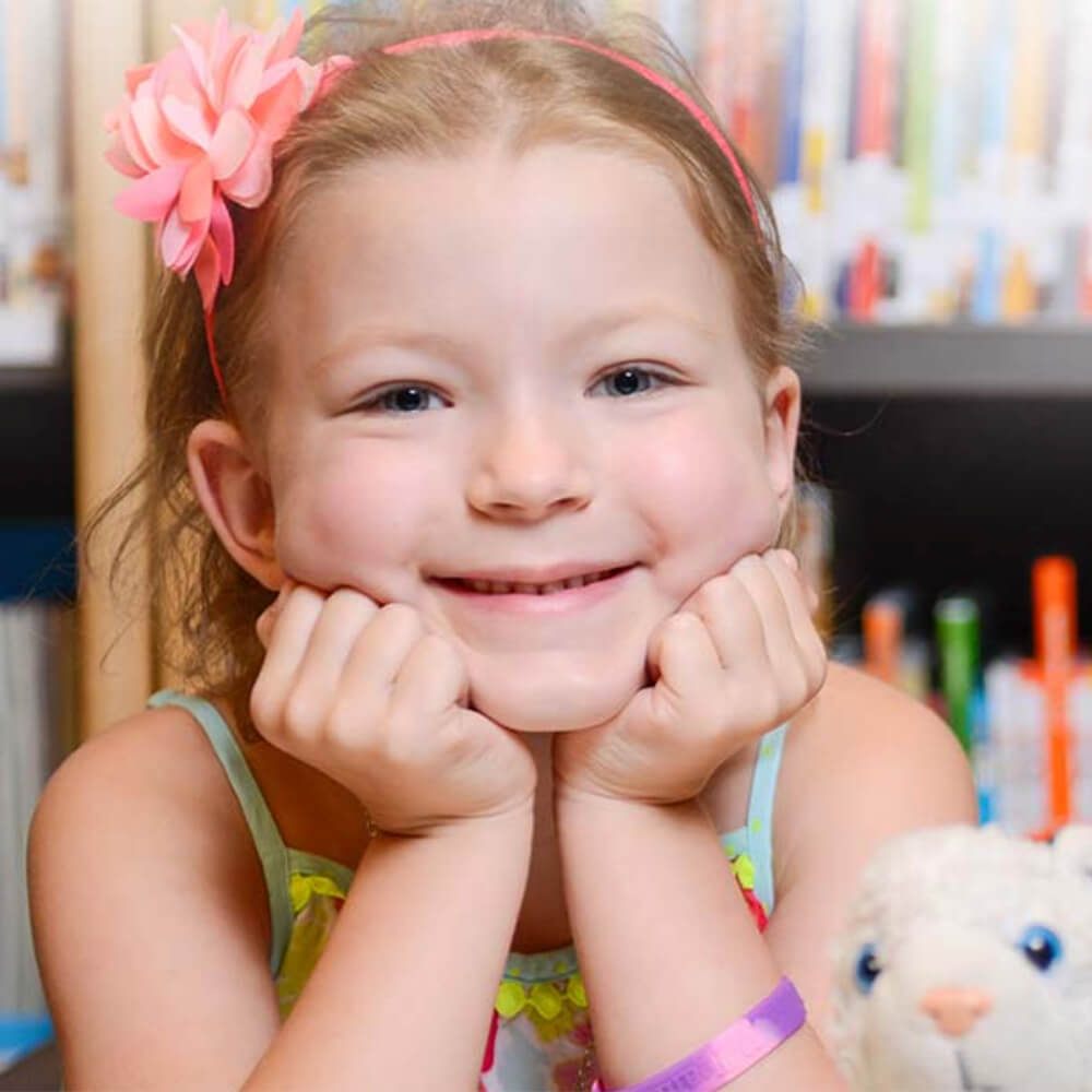 a young girl resting her face on her hands smiling at the camera